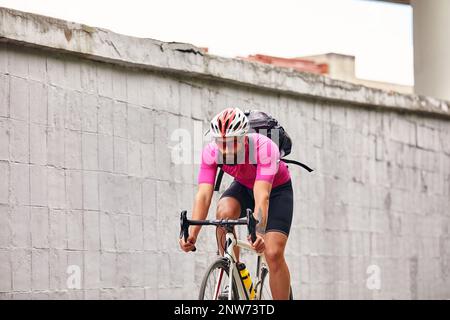 Ein Radfahrer mit Brille und Helm fährt durch die Stadt vor dem Hintergrund einer Betonwand Stockfoto
