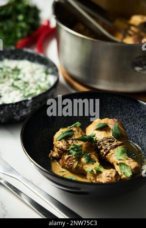 Afghanisches Huhn in scharfer Sauce mit Sahne und Joghurt. Salat mit Gurke und saurer Sahne im Hintergrund. Stockfoto