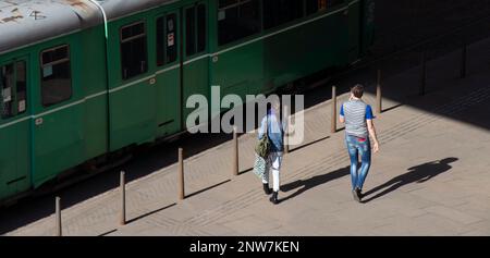 Belgrad, Serbien - 23. Februar 2023: Zwei junge Menschen nähern sich der grünen Straßenbahn an der Haltestelle für öffentliche Verkehrsmittel, hohe Rückansicht Stockfoto