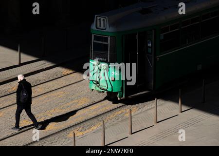 Belgrad, Serbien - 23. Februar 2023: Grüne Straßenbahn Nr. 11, die an der Bushaltestelle steht, und eine Person überquert eine Straße dahinter, hohe Rückansicht Stockfoto