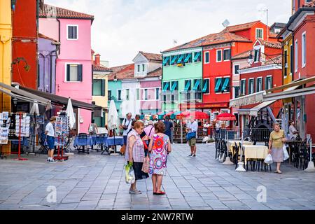 Ältere einheimische Frauen kaufen auf dem Platz mit bunten Restaurants in Burano, Insel in der Lagune von Venedig, Veneto, Norditalien Stockfoto