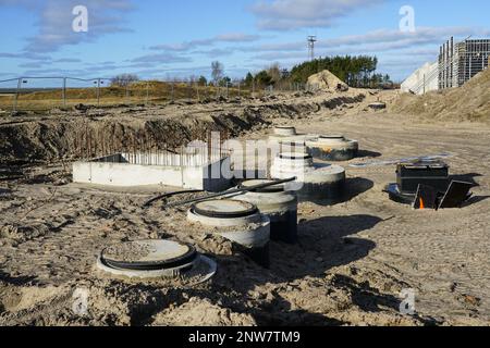 Bau unterirdischer Kommunikationsanlagen in einer neuen Industrieanlage, mehrere runde Stahlbetonbrunnen, blauer Himmel Stockfoto