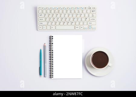 Arbeitsplatz mit Computertastatur, Notizblock, Stift, Bleistift und einer Tasse Kaffee oder Kakao auf weißem Hintergrund. Draufsicht, flaches Lay, Modell. Stockfoto