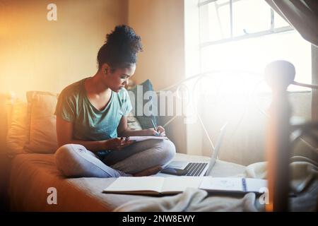 Eingetaucht in ihr Studienmaterial. Ganzkörperaufnahme einer jungen Studentin, die zu Hause studiert. Stockfoto