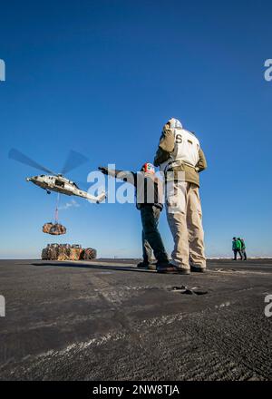 230108-N-EL850-1589 IONISCHES MEER (8. Januar 2023) Ein Matrose, der dem Flugzeugträger der Nimitz-Klasse USS George H.W. zugewiesen wurde Bush (CVN 77) signalisiert an einen MH-60s Nighthawk Helikopter, der an Helicopter Sea Combat Squadron (HSC) 5 angeschlossen ist, während einer Wiederauffüllung auf See mit dem Versorgungsschiff USNS Arctic (T-AOE 8), 8. Januar 2023. Carrier Air Wing (CVW) 7 ist die offensive Luft- und Streikkomponente der Carrier Strike Group (CSG) 10 und der George H.W. Buchse CSG. Die Geschwader von CVW-7 sind Strike Fighter Squadron (VFA) 143, VFA-103, VFA-86, VFA-136, Carrier Airborne Early Warning Squadron (V Stockfoto