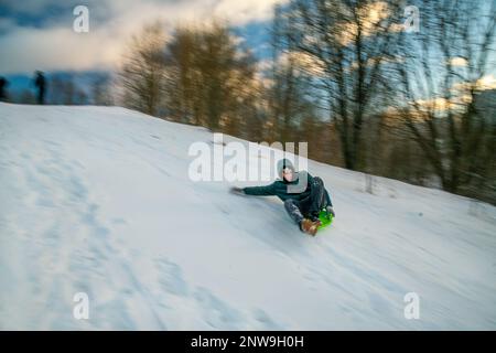 02-12-2022 Moskau Russland. Ein junger Mann, der auf einem Plastikschild von den Krylatsky-Hügeln in Moskau herunterrollt. Winter Februar in Russland. Stockfoto