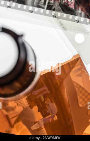 Detaildarstellung des schwarzen und weißen 35-mm-Filmstreifens und des farbigen Filmnegativs im 4x5-Format in transparenten Schutzhüllen neben einer Lupe auf einem Lichttisch. Stockfoto