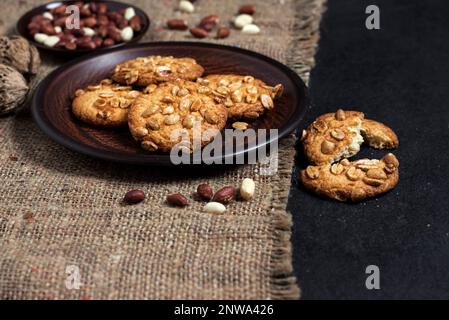 Hausgemachte Erdnusskekse auf einem braunen Teller mit rohen Erdnüssen im Hintergrund. Rustikales Essen Stockfoto