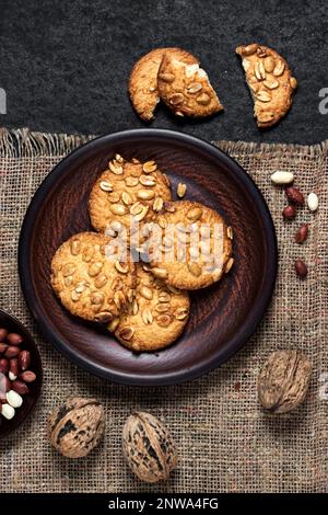 Hausgemachte Erdnusskekse auf einem braunen Teller mit rohen Erdnüssen im Hintergrund. Rustikales Essen. Flach liegend, Draufsicht Stockfoto