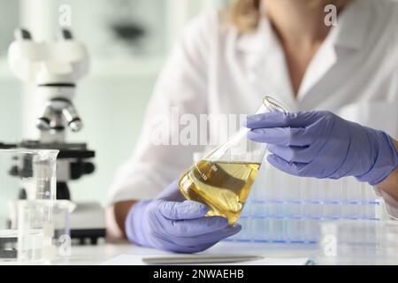 Eine Wissenschaftlerin, die eine Probe mit gelber Flüssigkeit hält Stockfoto