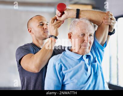 Seinen Weg zurück zu seinem gesunden selbst zu arbeiten. Aufnahme eines Physiotherapeuten, der einem älteren Mann mit Gewichten hilft. Stockfoto