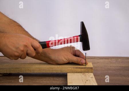 Bild eines handwerklichen Handwerkers, der beim Befestigen von Holzbohlen Hammer und Nägel hält. Stockfoto