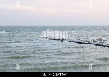 Nahaufnahme des eisigen Meeres, gefrorene Wellen, Felsen und Sonnenblendung auf dem Eis. Stockfoto