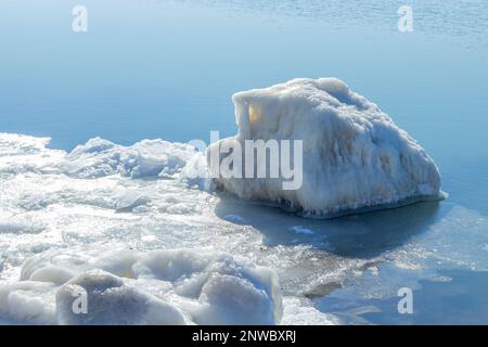 Nahaufnahme des eisigen Meeres, gefrorene Wellen, Felsen und Sonnenblendung auf dem Eis. Stockfoto