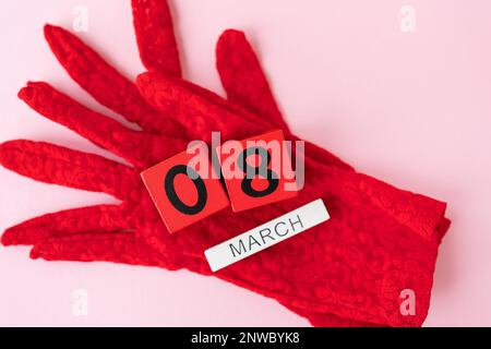 Wunderschöne rote Spitzenhandschuhe, die aus Holzwürfeln mit der Inschrift vom 8. März bestehen. Karte für den Feiertag, Frauentag Stockfoto