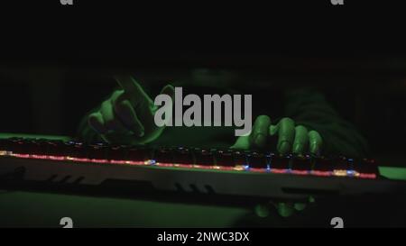 Farbige RGB-Tastatur, die Hacker oder Coder schreibt Code mit den Fingern auf grünes Licht Stockfoto