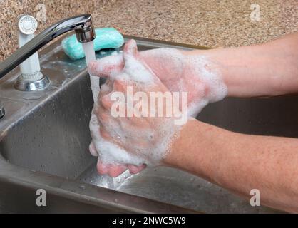 Horizontale Aufnahme einer Frau, die ihre Hände im Spülbecken wäscht, mit fließendem Wasser und einem Stück Seife auf dem Spülbrett. Stockfoto