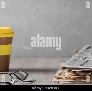 Morgen, bevor wir zur Arbeit gehen. Gemütliche Heimszene - ein Stapel alter Zeitungen, Gläser und ein Glas Kaffee auf einem Holztisch Stockfoto