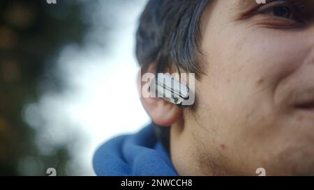 Lächelnder junger Mann mit Bluetooth-Ohrhörern, der Musik hört Stockfoto