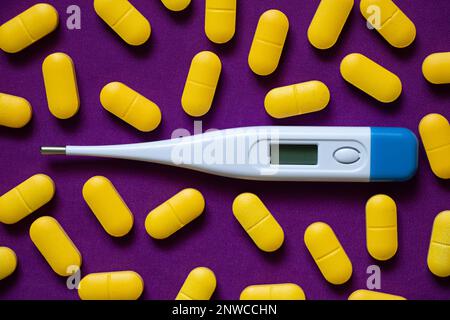 Elektronisches Thermometer liegt neben gelben Pillen auf einem isolierten Hintergrund, Medizin und Apotheke, Gesundheit und Behandlung, Pillen und Antibiotika Stockfoto