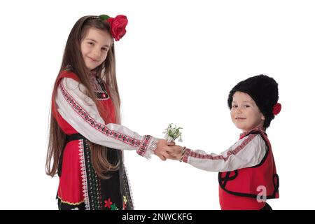 Bulgarische Kinder Junge, Mädchen in Folklore ethnischen Kostümen, Blumenstrauß Frühlingsblumen Schneeräume, Wolle Martenitsa Symbol für März Baba Marta Urlaub, Bulgarien Stockfoto