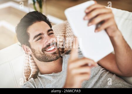 Komfortabel verbunden. Aufnahme eines jungen Mannes, der zu Hause drahtlose Technologie auf dem Sofa verwendet. Stockfoto