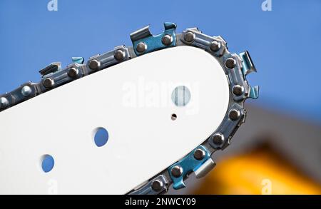 Details der Führungsschiene der Motorsäge. Scharfe Zähne auf glänzenden Stahlkettengliedern mit blauem Hintergrund. Nahaufnahme eines tragbaren Elektrowerkzeugs mit austauschbarem Schneidteil. Stockfoto