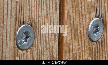 Lärchenbretter mit Holzschrauben aus Edelstahl auf Holzhintergrund. Verlegung von Naturplatten mit runden silbernen Köpfen aus selbstschneidenden Torx-Holzschrauben. Stockfoto