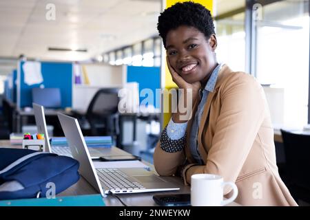 Porträt einer afroamerikanischen Geschäftsfrau, die ihren Laptop benutzt und im Büro lächelt. Arbeit im Büro, Geschäft, Finanzen und Unternehmenskonzept. Stockfoto