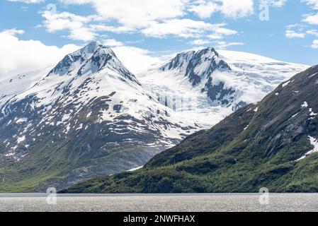 Atemberaubende, frische und perfekte schneebedeckte Berge im Sommer in Alaska mit Wolken, die einen teilweise blauen Himmel bedecken. Aufgenommen im Juni, Sommersaison. Stockfoto