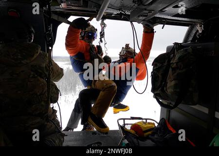 Alaska Air National Guard Staff Sgt. Kaden Wernofski, ein 210. Rettungsschwadron Special Missions Aviator, betreibt die Hebebühne, um 212. RQS Sanitäter in einen HH-60G Pave Hawk Helikopter zu heben, während einer Trainingsmission über dem unteren Susitna Valley bei Anchorage, Alaska, am 7. Februar 2023. Die HH-60G und das Rettungspersonal sowie ein 211. RQS HC-130J Combat King II-Flugzeug warten auf die Such- und Rettungsmission des Bundes in der riesigen arktischen Region Alaskas. Die Luftbetankungskapazität des HC-130F erweitert das Angebot des HH-60G Pave Hawk für Such- und Bergungsmissionen erheblich. Stockfoto