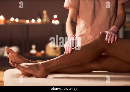 Asthetiker mit Zuckerpaste, um Körperbehaarung von Beinen junger Frauen zu entfernen Stockfoto