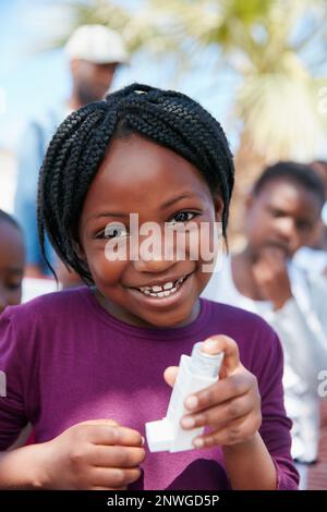 Ich kann jetzt leicht atmen. Porträt eines kleinen Mädchens, das einen Asthma-Inhalator bei einer Veranstaltung in der Gemeinde hält. Stockfoto