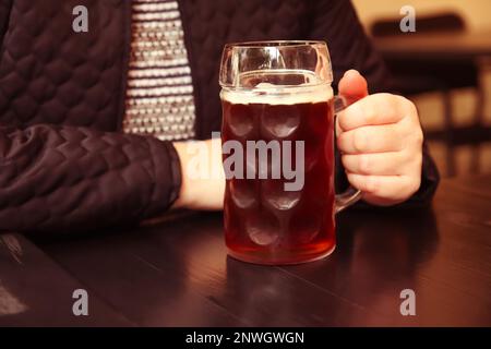 Dunkles Bier. Unschärfe-Tasse dunkles Bier. Eine Nahaufnahme zweier Hände, die Bier-steingläser klimpern. Leute, Frauen oder Männer, die Bier trinken. Bierhintergrund. Raus Stockfoto