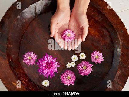 Entspannen Sie sich im Spa. Ein kurzer Schuss einer Frau reicht in einer mit Blumen gefüllten Wasserschale in einem Spa. Stockfoto