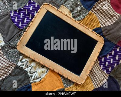 Leere handgehaltene Tafel auf violettem goldenem, altmodischem Steppstoff mit Platz für Text und Werbeschild. Die Decke ist handgefertigt. Stockfoto