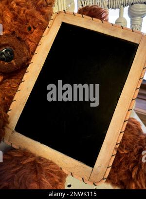 Die Tafel wird von einem großen braunen Teddybären gehalten. Es ist bereit für Ihre SMS, Nachricht, Ankündigung. Tafel ist altmodisch und mit Holzrahmen. Pelzbär ist groß. Stockfoto