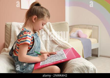 Kleine Mädchen malen Anti-Stress-Seite im Sessel drinnen Stockfoto