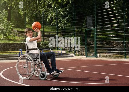 Behinderter Teenager im Rollstuhl, der Basketball auf dem Spielfeld spielt Stockfoto