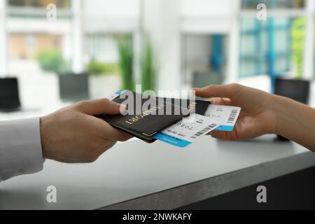 Ein Mitarbeiter, der einem Mann am Check-in-Schalter am Flughafen Pässe und Tickets gibt Stockfoto