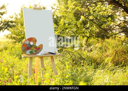 Hölzerne Staffelei mit leerer Leinwand und Malmaschinen auf der Wiese. Platz für Text Stockfoto