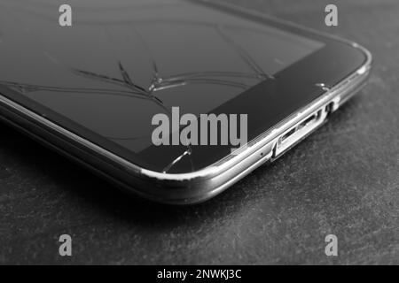 Smartphone mit rissigem Bildschirm auf schwarzem Tisch, Nahaufnahme. Gerätereparatur Stockfoto