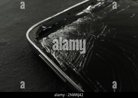 Smartphone mit rissigem Bildschirm auf schwarzem Tisch, Nahaufnahme. Gerätereparatur Stockfoto