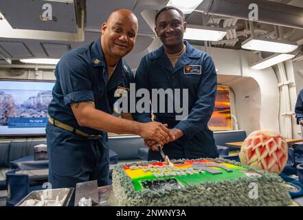 230217-N-NH267-1022 ARABISCHE SEE (17. Februar 2023) Kommandochef Damien Brown, Left und Retail Service Specialist Seaman Cedric Barnes schnitzte einen Kuchen an, um den Black History Month an Bord der geführten Raketenzerstörerin USS Paul Hamilton (DDG 60), 17. Februar 2023, im Arabischen Meer zu feiern. Paul Hamilton wird im US-Flottengebiet 5. eingesetzt, um die Sicherheit und Stabilität der Seeschifffahrt im Nahen Osten zu gewährleisten. Stockfoto