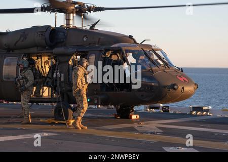 230124-N-XN177-2103 PAZIFIK (24. Januar 2023) – Besatzungsmitglieder wechseln ihre Position in den USA Army UH-60 Black Hawk Helikopter der 16. Kampfluftfahrtbrigade auf dem Flugdeck an Bord des amphibischen Angriffsträgers USS Tripoli (LHA 7), 24. Januar 2023. Tripoli führt gerade Routineeinsätze in der US-3.-Flotte durch. Stockfoto