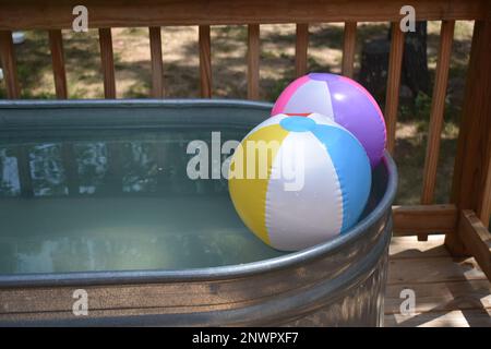 Zwei aufgeblasene Strandbälle, die in einem Stock-Tank-Pool schweben. Ein erfrischender Ort, um sich an einem heißen Sommertag abzukühlen. Stockfoto