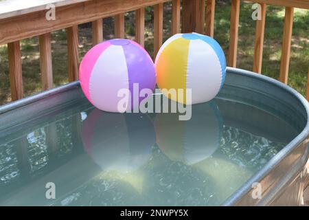 Zwei aufgeblasene Strandbälle, die in einem Stock-Tank-Pool schweben. Ein erfrischender Ort, um sich an einem heißen Sommertag abzukühlen. Stockfoto