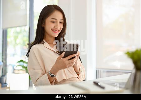 Charmante asiatische Geschäftsfrau oder Managerin, die ihr Telefon an ihrem Schreibtisch im Büro nutzt. Stockfoto