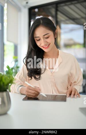 Porträt, charmante asiatische Millennials-Geschäftsfrau, die ein digitales Tablet an ihrem Schreibtisch im Büro verwendet. Geschäfts- und Technologiekonzept Stockfoto