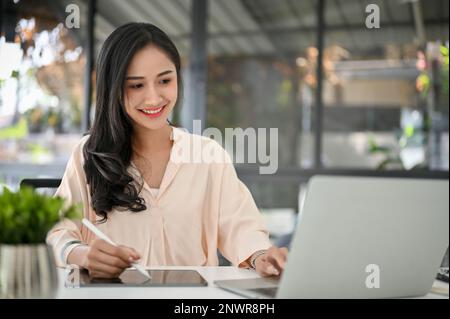 Professionelle und charmante asiatische Geschäftsfrau, die ein digitales Tablet und ein Notebook für ihre geschäftlichen Aufgaben im Büro verwendet. Stockfoto